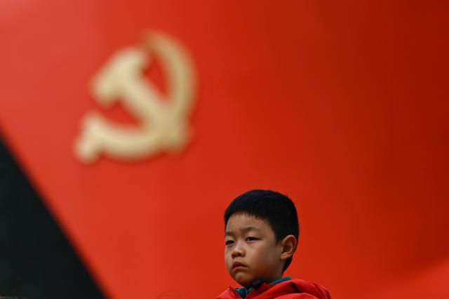 A boy watchs a Chinese New Year performance of traditional Chinese dances with a sculptural flag of the Communist Party seen in the background at the plaza of the Museum of the Communist Party of China in Beijing on March 1, 2026, ahead of the opening of the annual session of the National People's Congress (NPC). (Photo by Pedro PARDO / AFP)