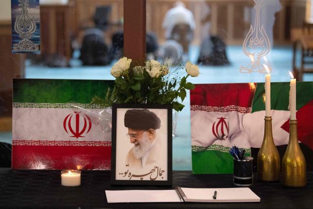 A portrait of Iran’s Supreme Leader Ayatollah Ali Khamenei is displayed next to Iranian flags, candles and a book of condolences at the Ahlul Bait Mosque Complex, while Muslim worshippers pray in his memory in Cape Town on March 01, 2026. Ayatollah Ali Khamenei, Iran's supreme leader since 1989 and sworn enemy of the West, was killed in the opening salvo of a massive US and Israeli attack, sparking a new wave of retaliatory missile strikes from Tehran on March 1, 2026. (Photo by RODGER BOSCH / AFP)
