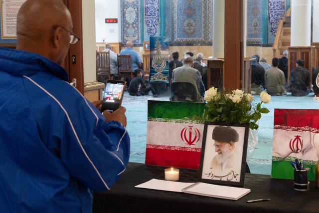 A man takes a photo of a portrait of Iran’s Supreme Leader Ayatollah Ali Khamenei as he stands with Iranian flags and candles at the Ahlul Bait Mosque Complex, while Muslim worshippers pray in his memory in Cape Town on March 01, 2026. Ayatollah Ali Khamenei, Iran's supreme leader since 1989 and sworn enemy of the West, was killed in the opening salvo of a massive US and Israeli attack, sparking a new wave of retaliatory missile strikes from Tehran on March 1, 2026. (Photo by RODGER BOSCH / AFP)