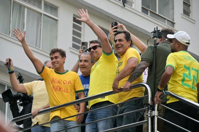 Brazilian Federal Deputy Nikolas Ferreira (L) and Senator and presidential candidate Flavio Bolsonaro (C) wave to supporters of Brazil's former president Jair Bolsonaro (2019-2022), sentenced to 23 years and 3 months for attempted coup, during a demonstration in Sao Paulo, Brazil, on March 1, 2026. (Photo by NELSON ALMEIDA / AFP)