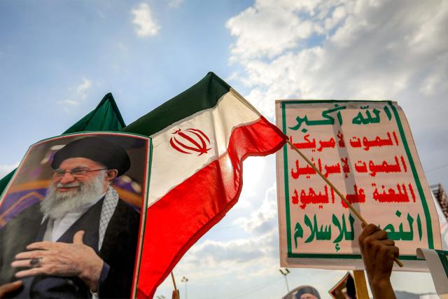 TOPSHOT - Mourners hold Iranian national flags and signs depicting Iran's supreme leader Ali Khamenei and "Sarkha" (Scream) slogan of Yemen's Huthis reading in Arabic "God is Great, death to America, death to Israel, curse upon the Jews, victory to Islam", during a memorial rally held by Huthi supporters a day after Khamenei was assassinated during US and Israeli strikes on Tehran, in the Huthi-held capital Sanaa on March 1, 2026. The United States and Israel launched strikes against Iran on February 28, killing Iran's supreme leader and top military leaders, prompting authorities to retaliate with strikes on Israel and US bases across the Gulf. (Photo by Mohammed HUWAIS / AFP)