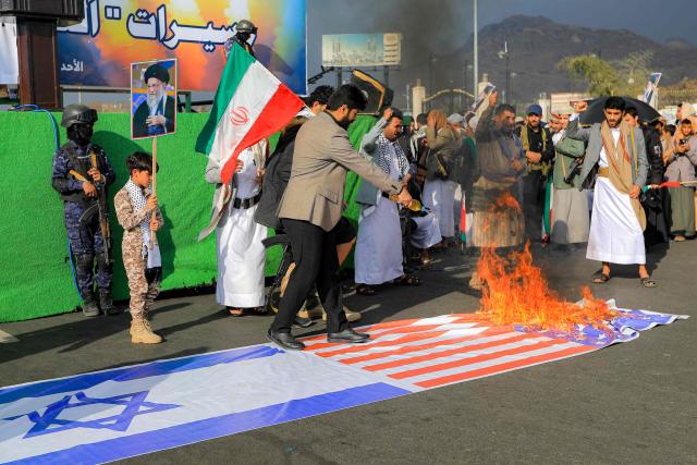 A man douses banners depicting the US and Israeli flags with fuel while set on fire during a memorial rally held by supporters of Yemen's Huthis a day after Iran's supreme leader was assassinated during a US and Israeli strikes on Tehran, in the Huthi-held capital Sanaa on March 1, 2026. The United States and Israel launched strikes against Iran on February 28, killing Iran's supreme leader and top military leaders, prompting authorities to retaliate with strikes on Israel and US bases across the Gulf. (Photo by Mohammed HUWAIS / AFP)