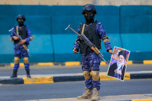 TOPSHOT - A masked fighter stands with a picture of Iran's supreme leader Ali Khamenei during a memorial rally held by supporters of Yemen's Huthis, a day after Khamenei was assassinated during US and Israeli strikes on Tehran, in the Huthi-held capital Sanaa on March 1, 2026. The United States and Israel launched strikes against Iran on February 28, killing Iran's supreme leader and top military leaders, prompting authorities to retaliate with strikes on Israel and US bases across the Gulf. (Photo by Mohammed HUWAIS / AFP)