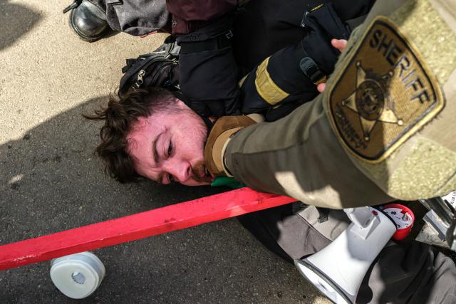 Law enforcement officers detain an activist outside the Bishop Henry Whipple Federal Building during a protest opposing US Immigration and Customs Enforcement (ICE) operations, in Minneapolis, Minnesota, on March 1, 2026. The demonstration was organized in connection with a prayer camp established across the street at the sacred site of Mni Owe Sni (Coldwater Spring), where Indigenous organizers have been gathering in recent weeks to pray for families affected by immigration enforcement and to call for “ICE out” and “Land Back.” Indigenous leaders say immigration enforcement and detention echo historic patterns of displacement and incarceration experienced by Native communities. The camp at Mni Owe Sni — considered a sacred Dakota site — was established to center ceremony, prayer and solidarity with immigrant families. (Photo by Kerem YUCEL / AFP)