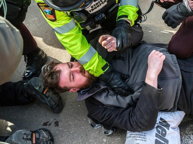 Law enforcement officers detain an activist outside the Bishop Henry Whipple Federal Building during a protest opposing US Immigration and Customs Enforcement (ICE) operations, in Minneapolis, Minnesota, on March 1, 2026. The demonstration was organized in connection with a prayer camp established across the street at the sacred site of Mni Owe Sni (Coldwater Spring), where Indigenous organizers have been gathering in recent weeks to pray for families affected by immigration enforcement and to call for “ICE out” and “Land Back.” Indigenous leaders say immigration enforcement and detention echo historic patterns of displacement and incarceration experienced by Native communities. The camp at Mni Owe Sni — considered a sacred Dakota site — was established to center ceremony, prayer and solidarity with immigrant families. (Photo by Kerem YUCEL / AFP)