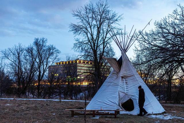A person walks past a teepee tent at the Indigenous-led prayer camp across from the Bishop Henry Whipple Federal Building in Minneapolis, Minnesota, on March 1, 2026. The prayer camp was established at the sacred site of Mni Owe Sni (Coldwater Spring), where Indigenous organizers have been gathering in recent weeks to pray for families affected by immigration enforcement and to call for "ICE out" and "Land Back." Indigenous leaders say immigration enforcement and detention echo historic patterns of displacement and incarceration experienced by Native communities. (Photo by Kerem YUCEL / AFP)
