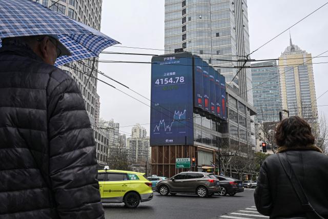 Pedestrians walk past a screen showing the Shanghai composite index in the Jing'an district of Shanghai on March 2, 2026. Oil prices soared and stocks fell in Asia on March 2 after US-Israeli strikes on Iran sent investors fleeing the prospect of an extended conflict in the crude-rich Middle East. (Photo by Jade GAO / AFP)