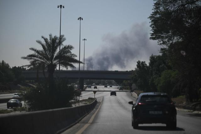 TOPSHOT - Motorists drive along a street as smoke rises from a reported Iranian strike in the area where the US Embassy is located in Kuwait City on March 2, 2026. Black smoke was seen rising from the US embassy in Kuwait City on March 2 after the latest volley of Iranian strikes, an AFP correspondent saw. (Photo by AFP)