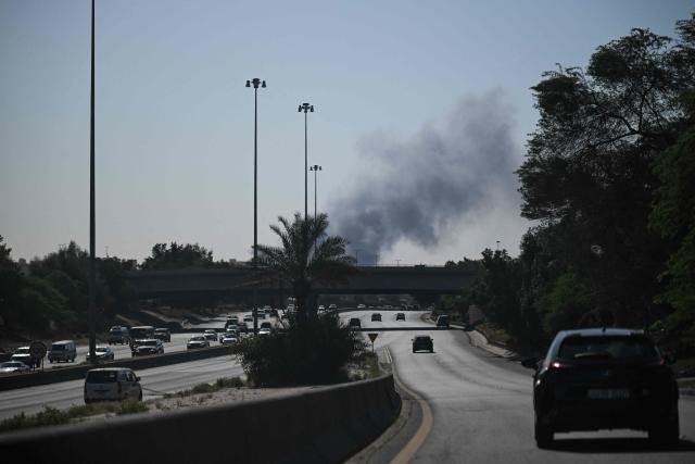 Motorists drive along a street as smoke rises from a reported Iranian strike in the area where the US Embassy is located in Kuwait City on March 2, 2026. Black smoke was seen rising from the US embassy in Kuwait City on March 2 after the latest volley of Iranian strikes, an AFP correspondent saw. (Photo by AFP)