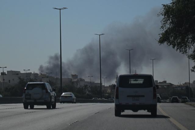 TOPSHOT - Motorists drive along a street as smoke rises from a reported Iranian strike in the area where the US Embassy is located in Kuwait City on March 2, 2026. Black smoke was seen rising from the US embassy in Kuwait City on March 2 after the latest volley of Iranian strikes, an AFP correspondent saw. (Photo by AFP)