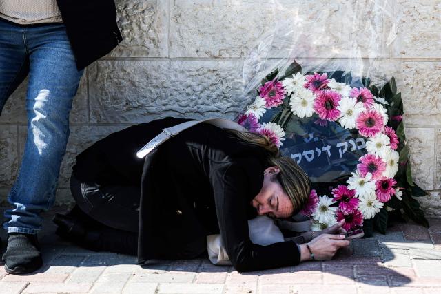 TOPSHOT - An Israeli woman huddles next to a wreath as she takes cover while war siren blast, during the funeral of Sarah and Ronit Elimelech, the day after a missile attack on Bet Shemesh killed several people, some 30 kilometres west of Jerusalem on March 2, 2026. A barrage of missiles launched from Iran killed at least six people in the central Israel city of Bet Shemesh on March 1, Israel's first responders agency, Magen David Adom (MDA) said, the day after the US and Israel attacked Iran and assassinated its supreme leader. (Photo by Ilia YEFIMOVICH / AFP)