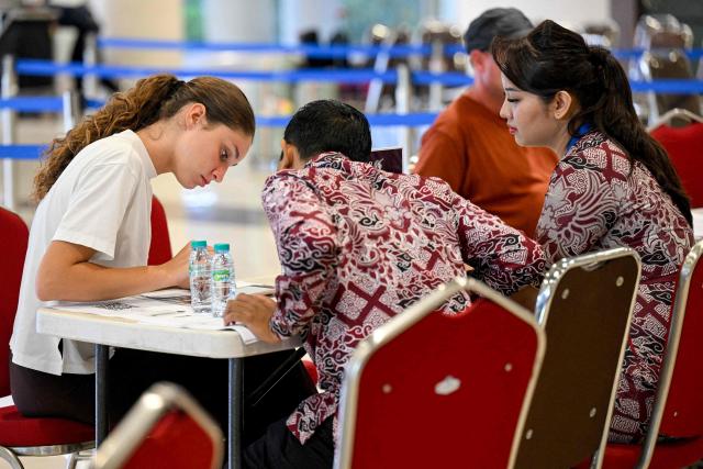 A passenger speaks to airport staff amid flights disruptions as a result of the Israeli-US strikes on Iran, at Ngurah Rai International Airport on Indonesia's resort island of Bali, on March 2, 2026. (Photo by SONNY TUMBELAKA / AFP)