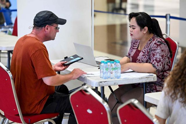 A passenger speaks to airport staff amid flights disruptions as a result of the Israeli-US strikes on Iran, at Ngurah Rai International Airport on Indonesia's resort island of Bali, on March 2, 2026. (Photo by SONNY TUMBELAKA / AFP)