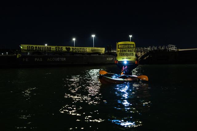 A Greenpeace activist holds a banner reading "Rosatom = Toxic contracts" as they take part in an operation to block the cargo ship Mikhail Dudin in Dunkirk, northern France on March 2, 2026. Greenpeace blocked a cargo ship in a lock at the port of Dunkirk (North) to prevent it from unloading its cargo, which the environmental NGO suspects is uranium from Russia intended for the French nuclear sector. The blocking of the cargo ship Mikhail Dudin, which began at 4:10 a.m. and was still underway at 8:00 a.m., was also confirmed by the police, who are also on site. (Photo by Sameer Al-DOUMY / AFP)