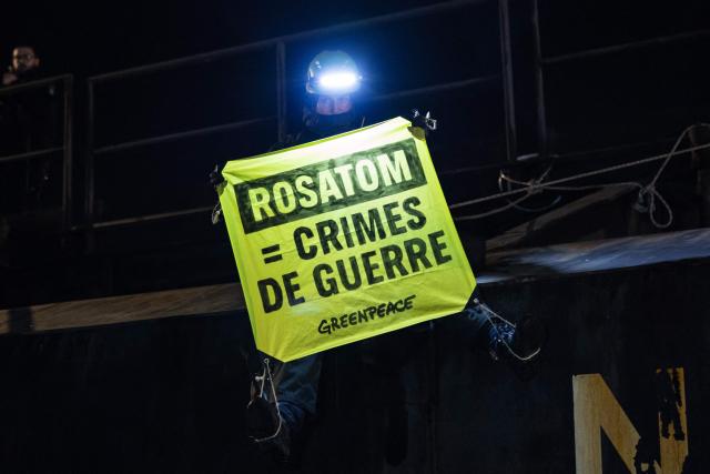 A Greenpeace activist holds a banner reading "Rosatom = War crimes" as they take part in an operation to block the cargo ship Mikhail Dudin in Dunkirk, northern France on March 2, 2026. Greenpeace blocked a cargo ship in a lock at the port of Dunkirk (North) to prevent it from unloading its cargo, which the environmental NGO suspects is uranium from Russia intended for the French nuclear sector. The blocking of the cargo ship Mikhail Dudin, which began at 4:10 a.m. and was still underway at 8:00 a.m., was also confirmed by the police, who are also on site. (Photo by Sameer Al-DOUMY / AFP)