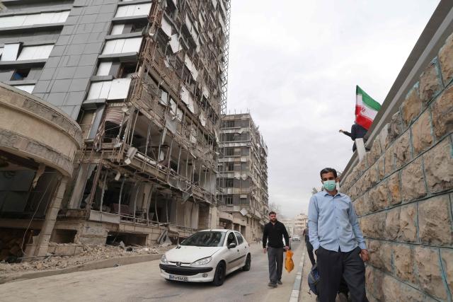 Iranians walk past the damaged Gandi Hospital, which was hit March 1, when a projectile struck a state TV communications tower and nearby buildings across the street, during the ongoing joint US-Israeli military campaign on the capital Tehran on March 2, 2026. The United States and Israel launched strikes against Iran on February 28, killing Iran's supreme leader and top military leaders, prompting authorities to retaliate with strikes on Israel and across the Gulf. (Photo by ATTA KENARE / AFP)