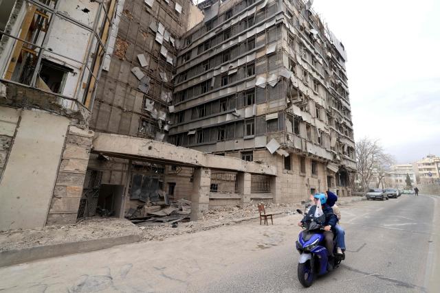 Iranian rider their moped past the damaged Gandi Hospital, which was hit March 1, when a projectile struck a state TV communications tower and nearby buildings across the street, during the ongoing joint US-Israeli military campaign on the capital Tehran on March 2, 2026. The United States and Israel launched strikes against Iran on February 28, killing Iran's supreme leader and top military leaders, prompting authorities to retaliate with strikes on Israel and across the Gulf. (Photo by ATTA KENARE / AFP)