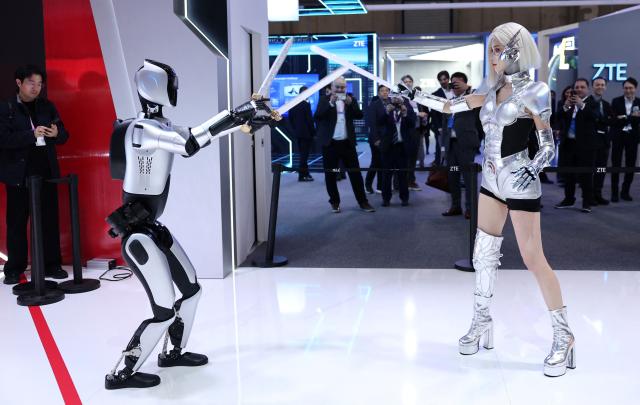 A picture taken on March 2, 2026 in Barcelona shows a ZTE robot pretending fighting with a woman at the Mobile World Congress (MWC), the world's biggest mobile technology showcase and fair. The Mobile World Congress (MWC), the major annual telecommunications event, opens today in Barcelona for an edition where Artificial Intelligence in telecommunications will take center stage in the debates. The event, which marking its twentieth anniversary, will host the world's leading telecommunications operators and numerous manufacturers. 109,000 industry professionals and visitors are expected. (Photo by Josep LAGO / AFP)