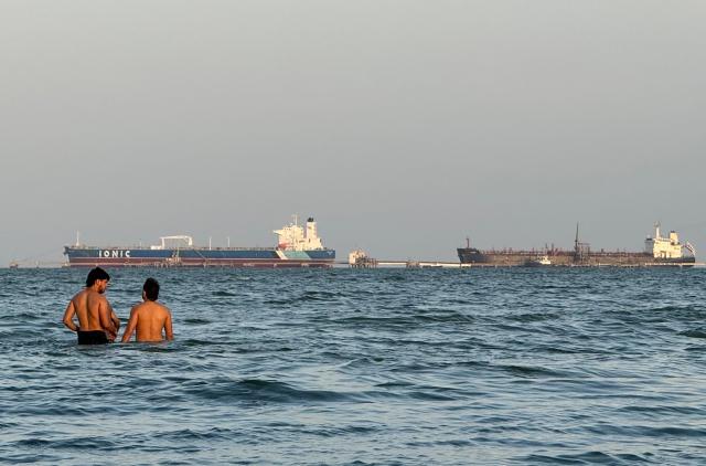People enjoy the water in front of oil tankers docked at Maracaibo Lake in Maracaibo, Venezuela, on March 1, 2026. Venezuela was once a major crude supplier to the US, and has the world's largest proven reserves with more than 303 billion barrels, according to global oil cartel OPEC. (Photo by Margioni BERMÚDEZ / AFP)