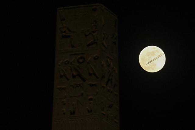 An aircraft flies past a full moon, seen next to the Luxor Obelisks at Place de la Concorde in Paris on March 2, 2026. (Photo by Christophe DELATTRE / AFP)