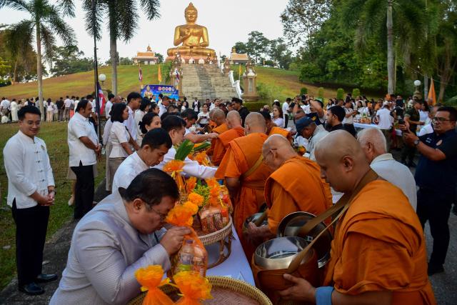 Buddhist devotees offer food to monks near a giant Buddha statue during an event to mark Makha Bucha Day in the southern Thai town of Narathiwat on March 3, 2026. (Photo by Madaree TOHLALA / AFP)