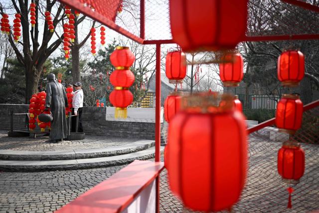 A woman poses for a picture with bronze statues decorated with lanterns at the entrance of an alley during the Lantern Festival in Beijing  on March 3, 2026. (Photo by WANG Zhao / AFP)