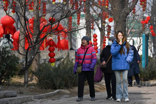 People walk along a road decorated with lanterns during the Lantern Festival in Beijing  on March 3, 2026. (Photo by WANG Zhao / AFP)