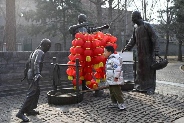 A child looks at a bronze statue decorated with lanterns at the entrance of an alley during the Lantern Festival in Beijing  on March 3, 2026. (Photo by WANG Zhao / AFP)