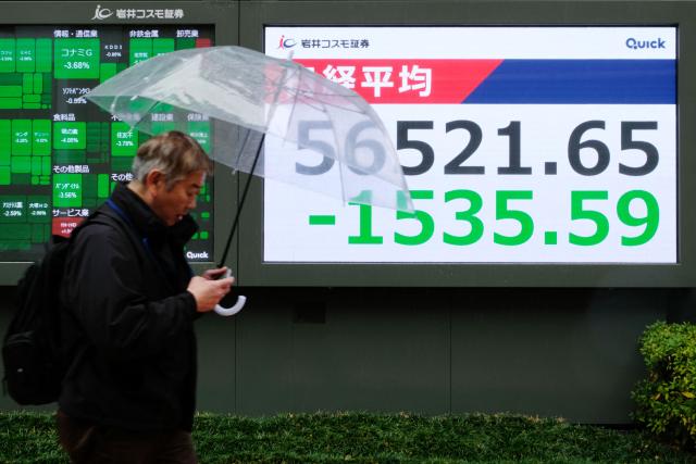 A man walks past an electronic quotation board displaying numbers of the Nikkei Stock Average on the Tokyo Stock Exchange along a street in Tokyo on March 3, 2026. (Photo by Kazuhiro NOGI / AFP)
