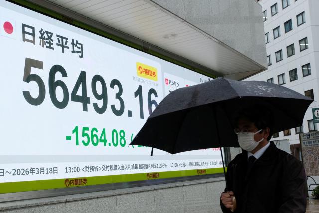 A man walks past an electronic quotation board displaying numbers of the Nikkei Stock Average on the Tokyo Stock Exchange along a street in Tokyo on March 3, 2026. (Photo by Kazuhiro NOGI / AFP)