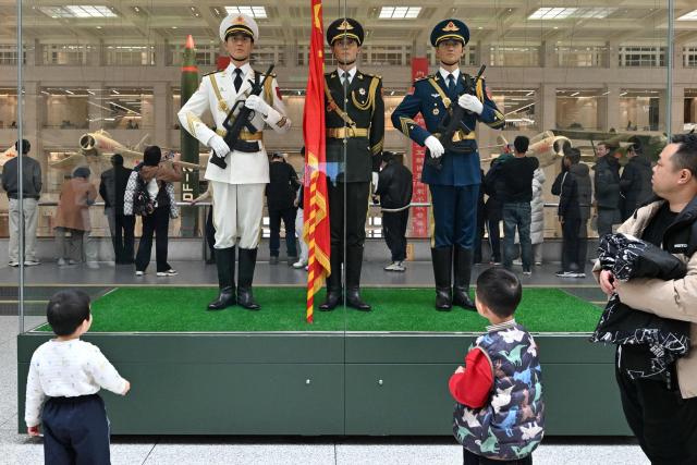Visitors look at an exhibit depicting soldiers in the service uniforms of the navy, ground, and air force branches of the Chinese People's Liberation Army at the Military Museum in Beijing on March 3, 2026, ahead of the opening of the annual session of the National People’s Congress (NPC). (Photo by ADEK BERRY / AFP)