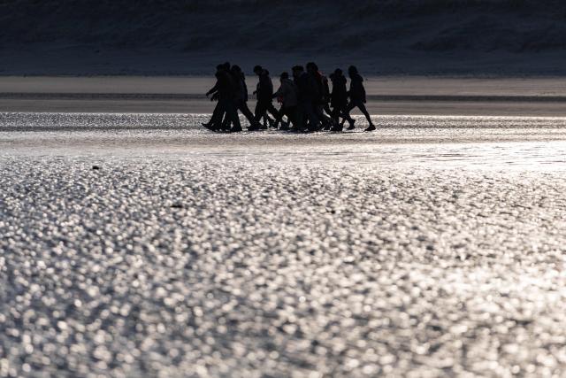 Migrants walk on the beach as they try to board a smugglers' boat in an attempt to cross the English Channel off the beach of Gravelines, northern France, on March 3, 2026. At dawn on March 3, 2026, four makeshift boats left the beach at Gravelines, each carrying at least around fifty people, taking advantage of the temporary improvement in weather conditions to attempt an illegal crossing of the English Channel, AFP journalists observed. (Photo by Sameer Al-DOUMY / AFP)