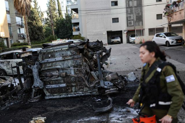 A member of the Israeli security forces walks past the wreckage of cars at a site struck by a projectile in Ramat Gan near Tel Aviv on March 3, 2026. The Middle East has becomed gripped by a war triggered by US and Israel launched airstrikes against Iran on February 28, that killed the Islamic republic's supreme leader and other officials. (Photo by Ilia YEFIMOVICH / AFP)