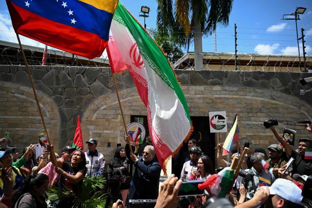 Iran's Ambassador to Venezuela, Ali Chegini (C), holds up an Iranian flag during a protest in solidarity with the Islamic Republic of Iran following armed conflict with the United States and Israel outside the Iranian embassy in Caracas on March 3, 2026. (Photo by Federico PARRA / AFP)