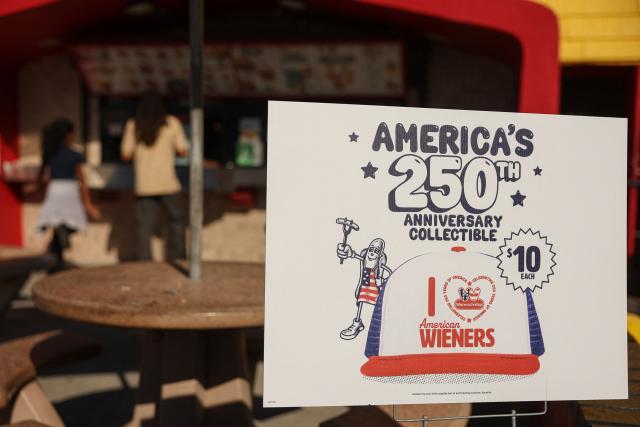 An America’s 250th anniversary hat sign is displayed as customers wait for food orders outside the Wienerschnitzel American hot dog and fast food restaurant in Los Angeles, on March 2, 2026. (Photo by Patrick T. Fallon / AFP)