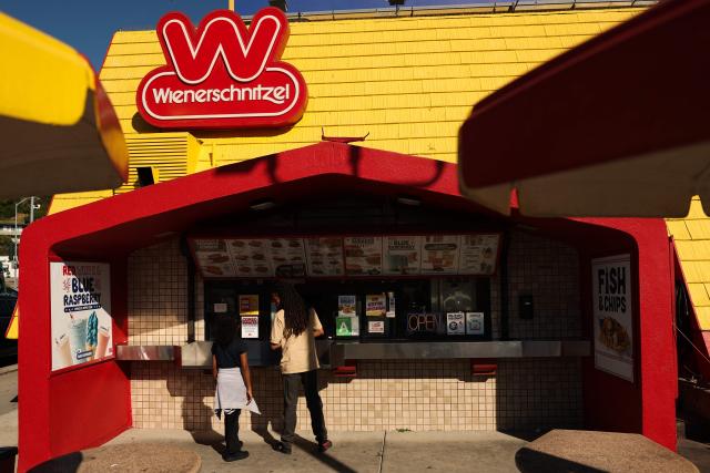 Customers wait for food orders as the Wienerschnitzel logo is displayed outside the A-frame roof of the American hot dog and fast food restaurant in Los Angeles, on March 2, 2026. (Photo by Patrick T. Fallon / AFP)