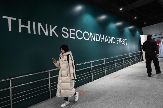 The photo taken on February 10, 2026 shows people walking past a slogan which reads "Think Secondhand First" outside a second-hand store in Shanghai. Boosting domestic consumption will be among key goals set forth by China's leaders at the annual Two Sessions political conclave this week, but they face an uphill battle. (Photo by Jade GAO / AFP) / To go with AFP story:  China-economy-politics-consumer-travel-retail, FOCUS by Jing Xuan TENG and Peter CATTERALL
