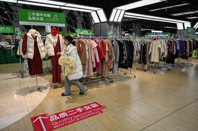 The photo taken on February 10, 2026 shows a woman walking past the clothes section at a second-hand store in Shanghai. Boosting domestic consumption will be among key goals set forth by China's leaders at the annual Two Sessions political conclave this week, but they face an uphill battle. (Photo by Jade GAO / AFP) / To go with AFP story:  China-economy-politics-consumer-travel-retail, FOCUS by Jing Xuan TENG and Peter CATTERALL