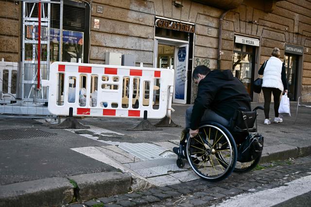 Italian lawyer Alessandro Bardin navigates a damaged ramp to access the sidewalk under reapair after crossing a cobblestone street in Rome on February 25, 2026. Paralympic organisers and Italy's government have invested tens of millions of euros in making the venues and areas around the Milan-Cortina Paralympic Games more accessible for people with disabilities. But the story is not the same across Italy, particularly in the capital Rome, known as much for its uneven roads and anarchic parking as for its ancient ruins. (Photo by Filippo MONTEFORTE / AFP)