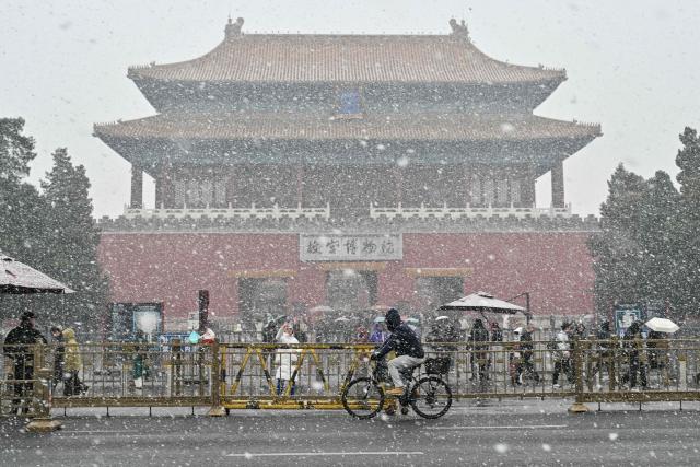 People stand outside the Forbidden city as it snows in Beijing on March 4, 2026. (Photo by Adek BERRY / AFP)