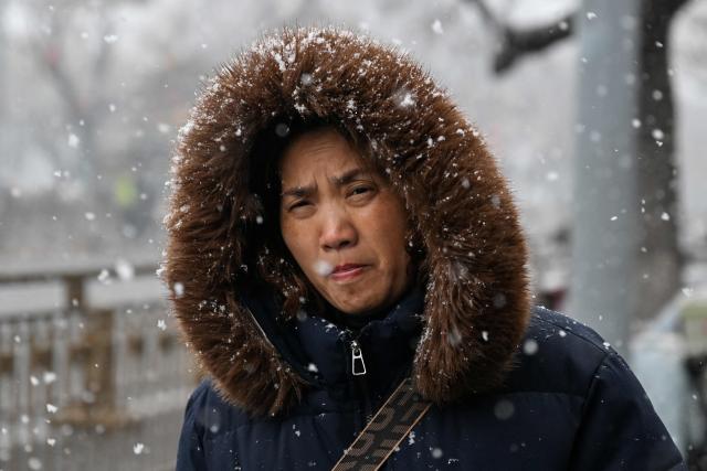 A woman walks along a road as it snows in Beijing on March 4, 2026. (Photo by Adek BERRY / AFP)