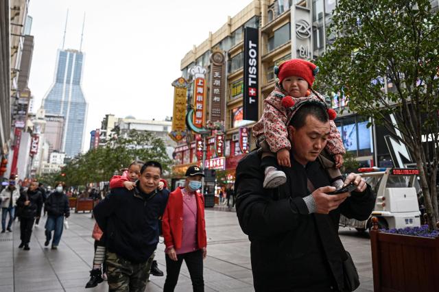 A man (R) carrying a baby on his shoulders walks on the Nanjing Road Pedestrian Street in Shanghai on March 4, 2026. (Photo by Jade GAO / AFP)