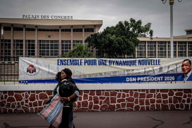 Women walk past an electoral poster of Congo-Brazzaville's 82-year-old President Denis Sassou Nguesso outside the Convention Center in Brazzaville on March 3, 2026, ahead of the country's March 15 presidential election. Congo-Brazzaville, a former French colony which gained independence in 1960, is rich in oil but nearly half of its six million people live below the poverty line. (Photo by Glody MURHABAZI / AFP)