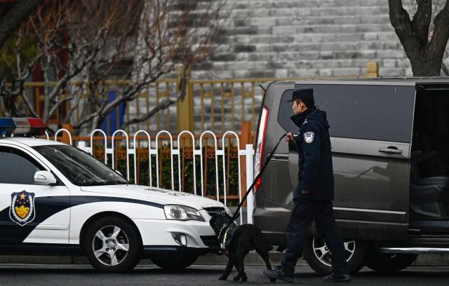 A police dog and its handler patrol in a street surrounding the Great Hall of the People where the opening of the Chinese People's Political Consultative Conference (CPPCC) takes place, in Beijing on March 4, 2026. (Photo by Pedro PARDO / AFP)