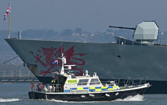 A Police patrol boat passes HMS Dragon, a Royal Navy Type 45 Daring-class air-defence destroyer warship, moored outside HM Naval Base Portsmouth, on the south coast of England, on March 4, 2026. British Prime Minister Keir Starmer said March 3, 2026 that the UK was dispatching "helicopters with counter drone capabilities" and a warship, HMS Dragon, to Cyprus as Britain continues "defensive operations" in the region. His announcement comes after Britain's Royal Air Force (RAF) Akrotiri base was struck early Monday by an Iranian-made drone, which hit the runway. (Photo by JUSTIN TALLIS / AFP)