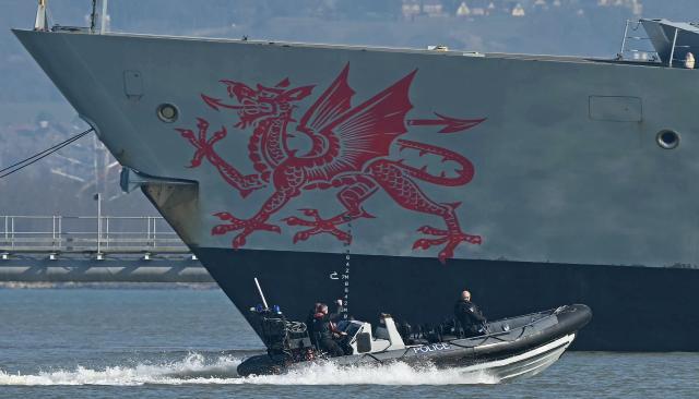 A Police patrol boat passes HMS Dragon, a Royal Navy Type 45 Daring-class air-defence destroyer warship, moored outside HM Naval Base Portsmouth, on the south coast of England, on March 4, 2026. British Prime Minister Keir Starmer said March 3, 2026 that the UK was dispatching "helicopters with counter drone capabilities" and a warship, HMS Dragon, to Cyprus as Britain continues "defensive operations" in the region. His announcement comes after Britain's Royal Air Force (RAF) Akrotiri base was struck early Monday by an Iranian-made drone, which hit the runway. (Photo by JUSTIN TALLIS / AFP)