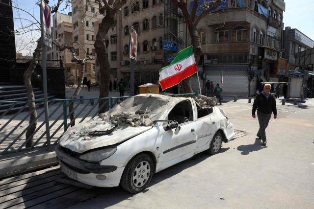 A man walks past an Iranian flag fluttering above the wreckage of a car in central Tehran, on March 4, 2026. Iran's Revolutionary Guards said on March 4, they had total control of the Strait of Hormuz, a key waterway for global energy transit, as Israel launched a new wave of strikes on the Iranian capital. (Photo by AFP)