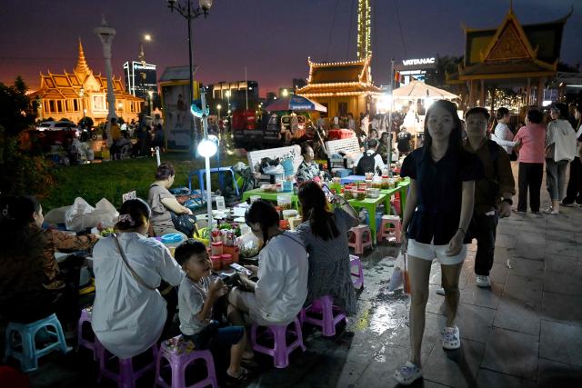 Pedestrians walk past people eating food near the Royal Palace in Phnom Penh on March 4, 2026. (Photo by TANG CHHIN Sothy / AFP)