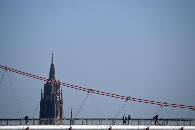 People cross the Holbeinsteg pedestrian bridge over the Main river in Frankfurt am Main, western Germany, on March 4, 2026 as the air temperature reached 15 degrees Celsius above zero. (Photo by Kirill KUDRYAVTSEV / AFP)