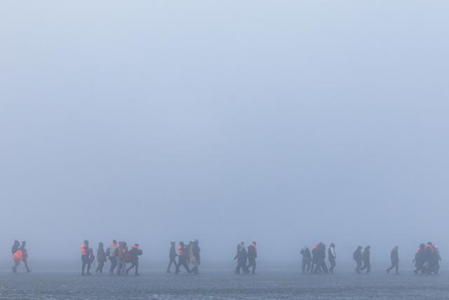 Migrants walk in a foggy weather to try to board a smugglers' boat in an attempt to cross the English Channel off the beach of Gravelines, northern France, on March 4, 2026. (Photo by Sameer Al-DOUMY / AFP)